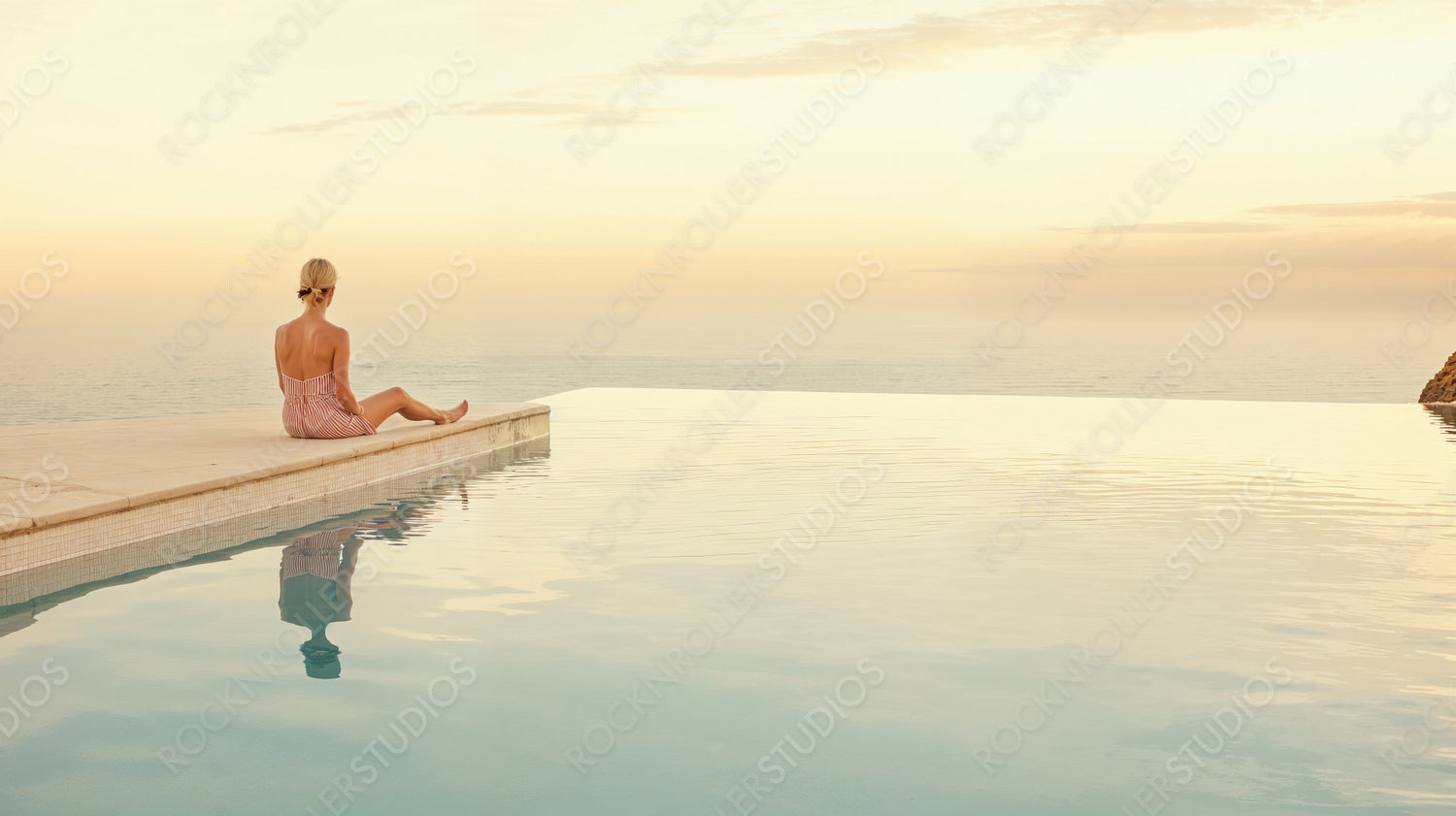Serene Sunset Escape: Woman by Infinity Pool Overlooking the Sea